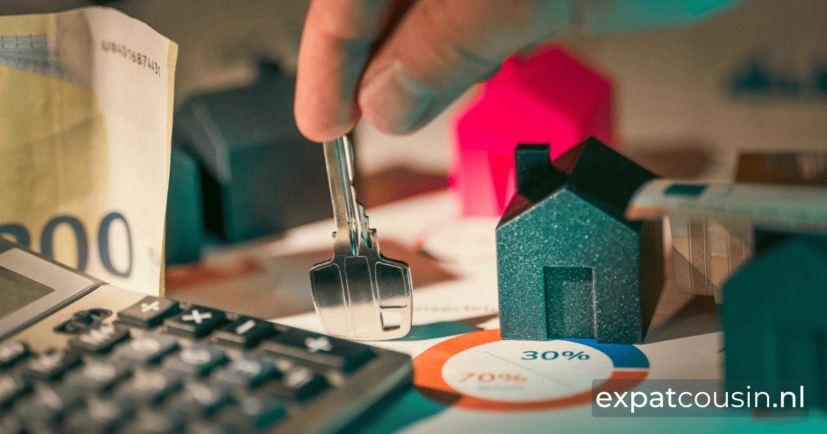 A house key is being held up vertically by an index finger and thumb between little plastic houses. To the left a calculator below a money note.